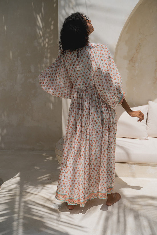 Daughters of India Kyra Maxi Dress in Coral — back view in courtyard, gathered waist and border hem, palm shadows