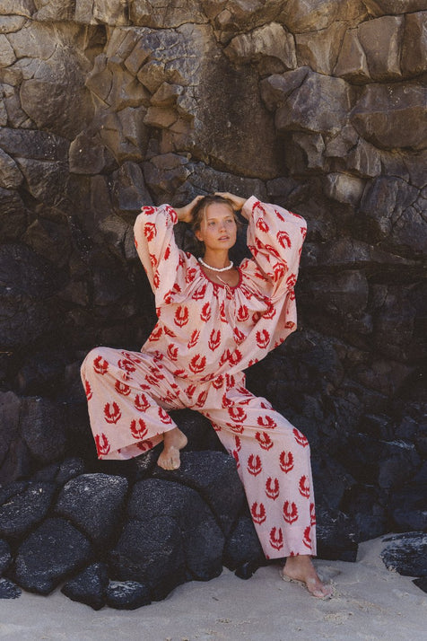 Ria Pants Cherry Blossom — outdoor rocky setting portrait, model wearing cherry blossom hand block print cotton wide-leg pants, pink floral motif on cream, barefoot styling, artisan Jaipur India | Daughters of India